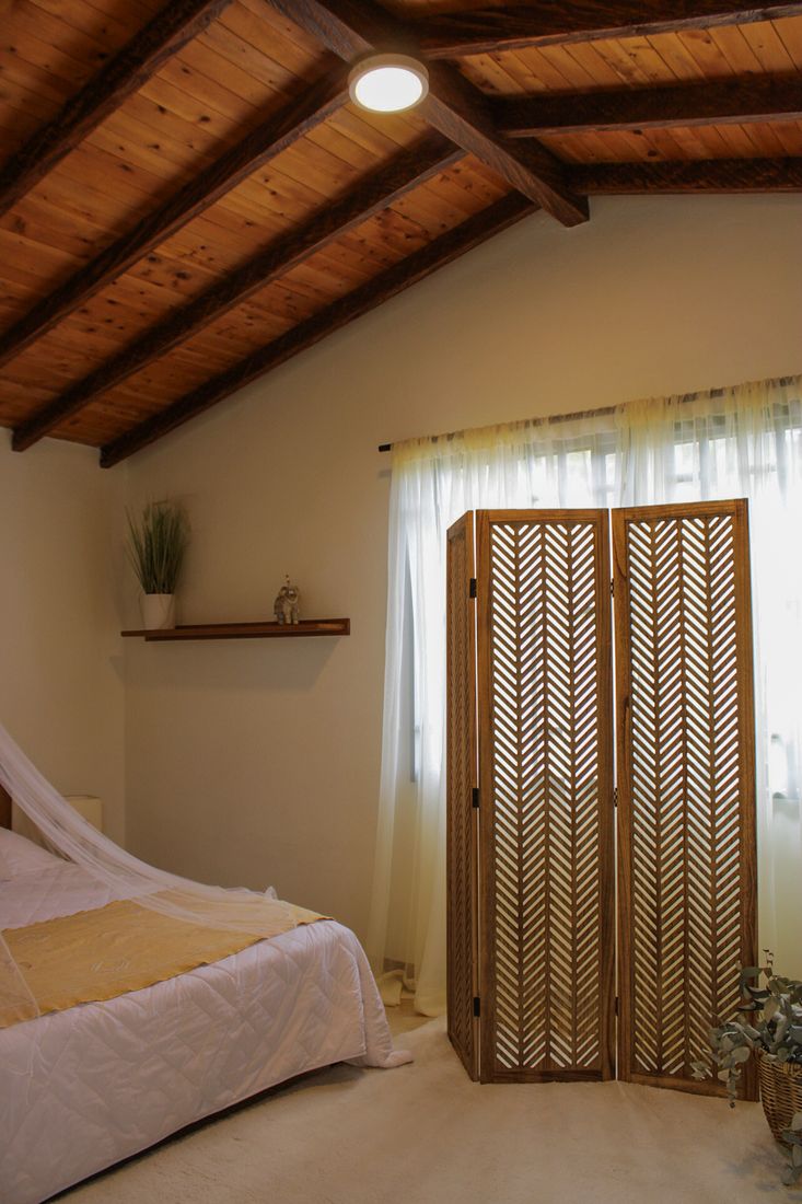 Detalle de biombo de madera tallado y cortinas de lino en dormitorio de Casa Taná